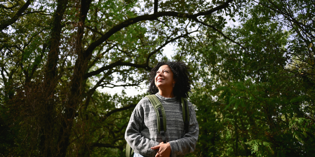 multiracial woman with curly hair standing in a woodland and admiring the nature.